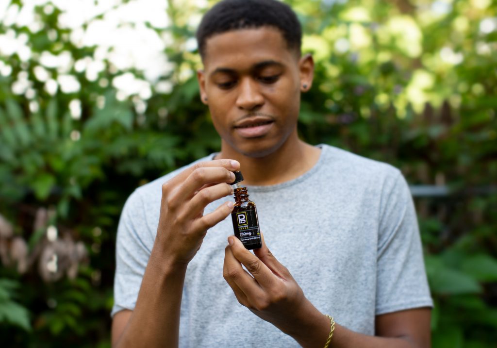 Tyler Jurelle’s face is visible as he displays a Physicians Grade CBD product, focusing on its premium packaging.