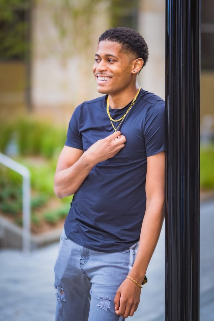 Tyler Jurelle admiring his Craftd London jewelry, including a rope gold chain and St. Christopher pendant, in Downtown Jersey City, captured by Aaron Robinson.