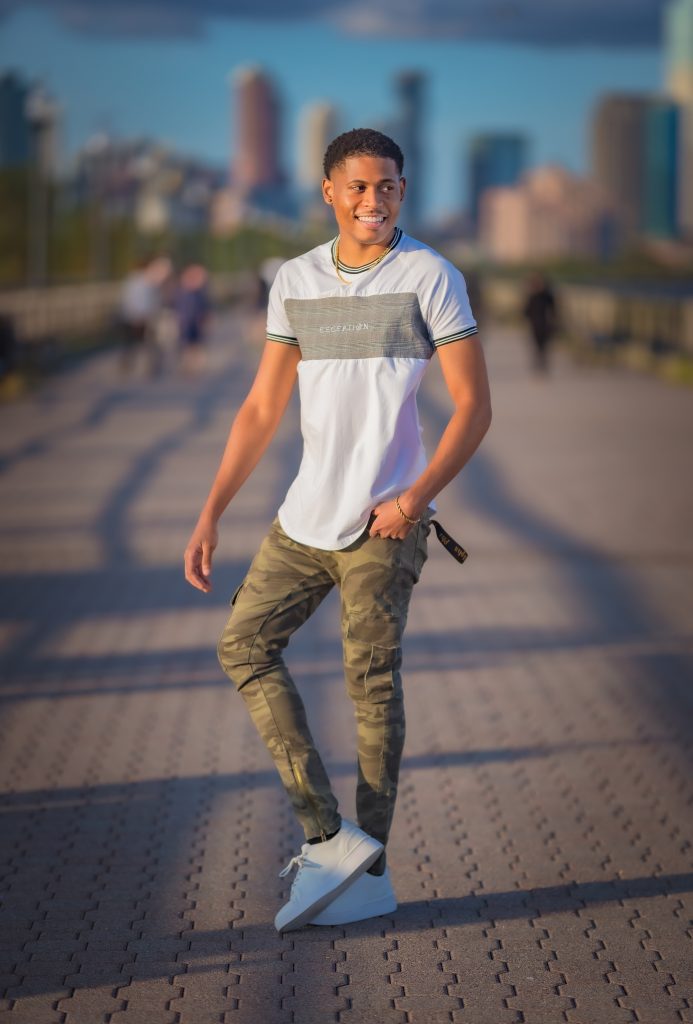 Full-body shot of Tyler Jurelle wearing a Deception Toronto Miami Plaid Tee, Cesar Military Cargo Jeans, and Zara sneakers at Liberty State Park.