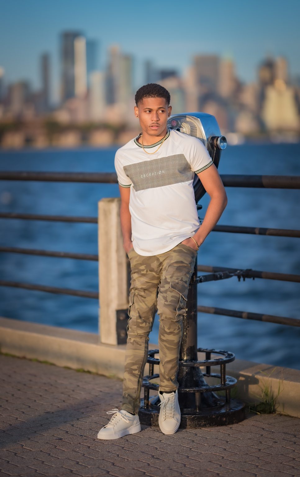 Full-body shot of Tyler Jurelle wearing a Deception Toronto Miami Plaid Tee, Cesar Military Cargo Jeans, and Zara white sneakers at Liberty State Park in Jersey City.