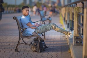 Tyler Jurelle sitting at Liberty State Park, showcasing Deception Toronto Cesar Military Cargo Jeans and Zara white sneakers. Check out his Deception Toronto review and recommendations.