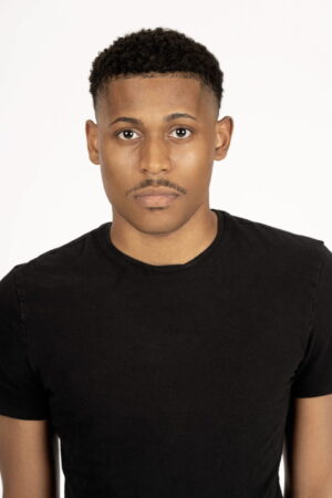 Headshot of Tyler Jurelle in an all-black outfit against a white backdrop, showcasing a bold and minimalist look.