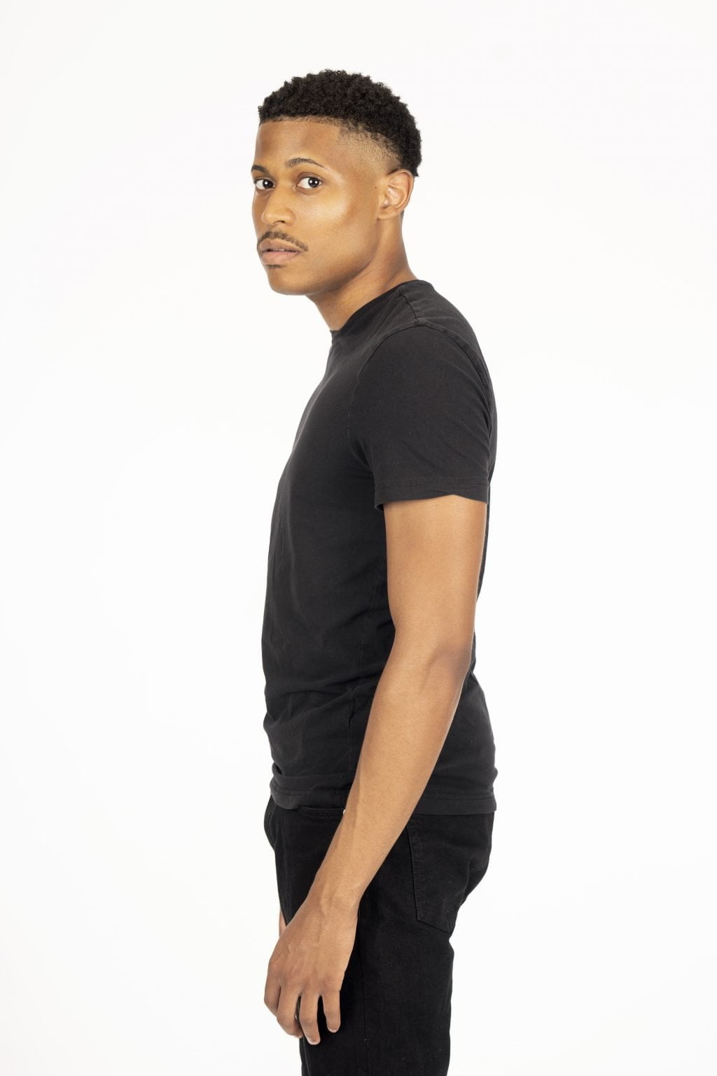 3/4 body side profile shot of Tyler Jurelle in an all-black outfit, standing against a white backdrop.