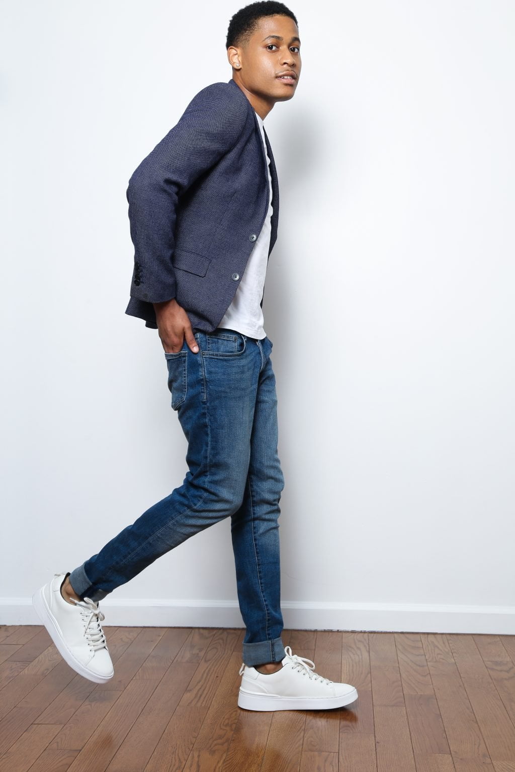 The full-body shot of Tyler Jurelle standing in blue jeans, a white t-shirt, and a slim blue blazer exemplifies modern urban fashion.