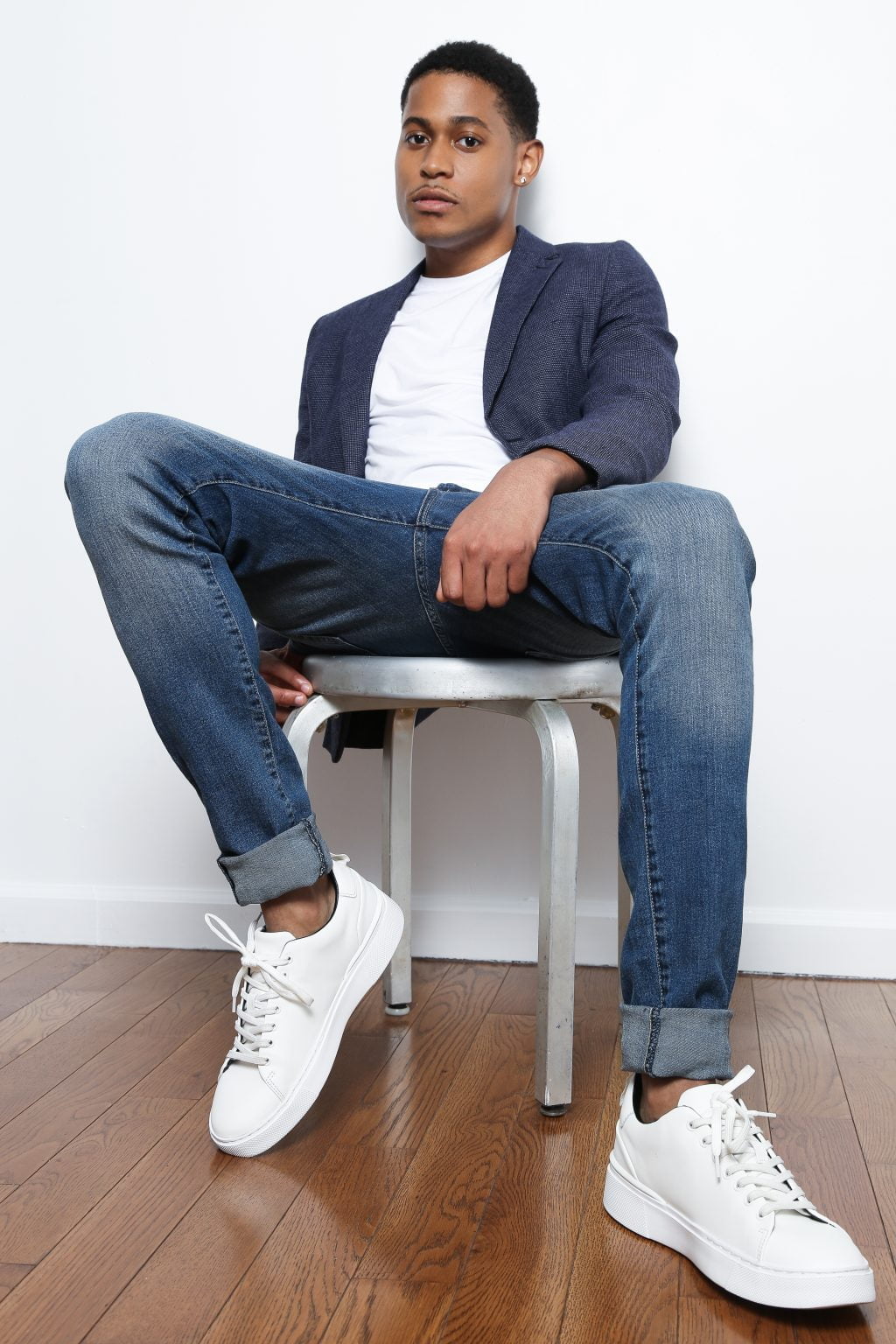 Tyler Jurelle sits confidently in blue jeans, a plain white t-shirt, and a blue slim blazer, showcasing a blend of casual and refined style.