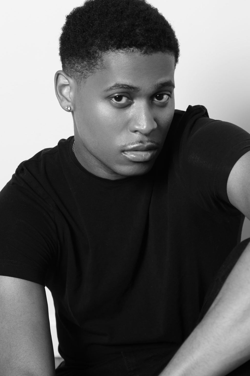 Tyler Jurelle in a plain black t-shirt, sitting on the floor, captured in a thoughtful black and white headshot by Jorge Pagan Jr.