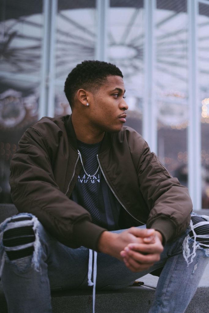 Men's fashion creator Tyler Jurelle is relaxing at Brooklyn Bridge Park in Biker Patch Denim and a green bomber jacket.