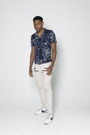 A full-body shot captures male model Tyler Jurelle showing confidence in a blue summer button-up and NVLTY London’s beige biker cargo pants.
