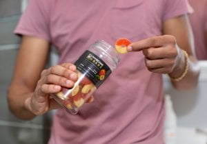 Tyler Jurelle holds a bottle of Physicians Grade CBD gummies in one hand and a single gummy in the other, highlighting the product.