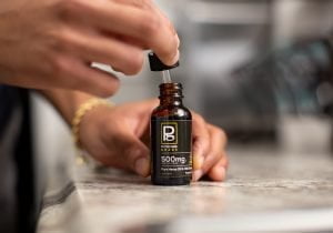 A hand demonstrates the dropper of a Physicians Grade CBD tincture, showcasing its practical use.