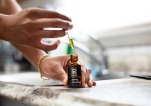 Close-up of a hand holding a Physicians Grade CBD oil bottle, focusing on the product’s details.