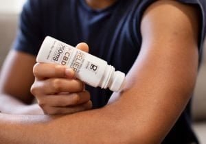 Hand applying Physicians Grade CBD balm on the opposite arm, highlighting its smooth texture.