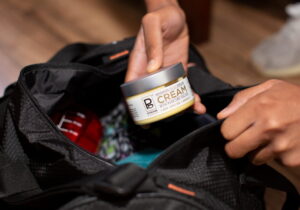 A close-up of Tyler Jurelle holding a jar of Physicians Grade CBD cream after removing it from the duffle bag, focusing on the product.