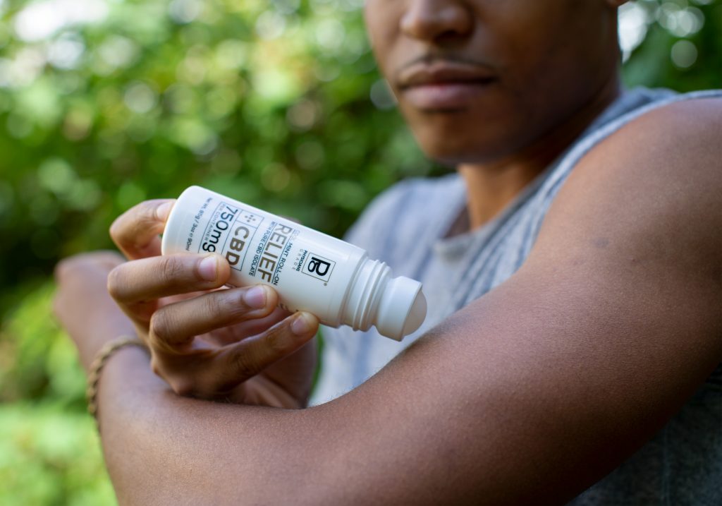 Men's lifestyle creator Tyler Jurelle is holding a Physicians Grade CBD balm jar and applying it to his opposite arm, emphasizing its high-quality features.