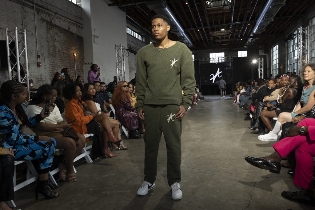 A moment on the runway, men's fashion model Tyler Jurelle is ready and styled in a wool crewneck and sweatpants set by Vaughn Acquis.