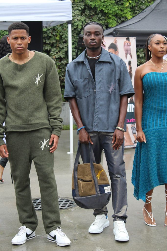 In a group shot with other models, Tyler Jurelle is wearing a stylish khaki green wool set while other models are rocking gear designed by Vaughn Acquis before walking on the runway.
