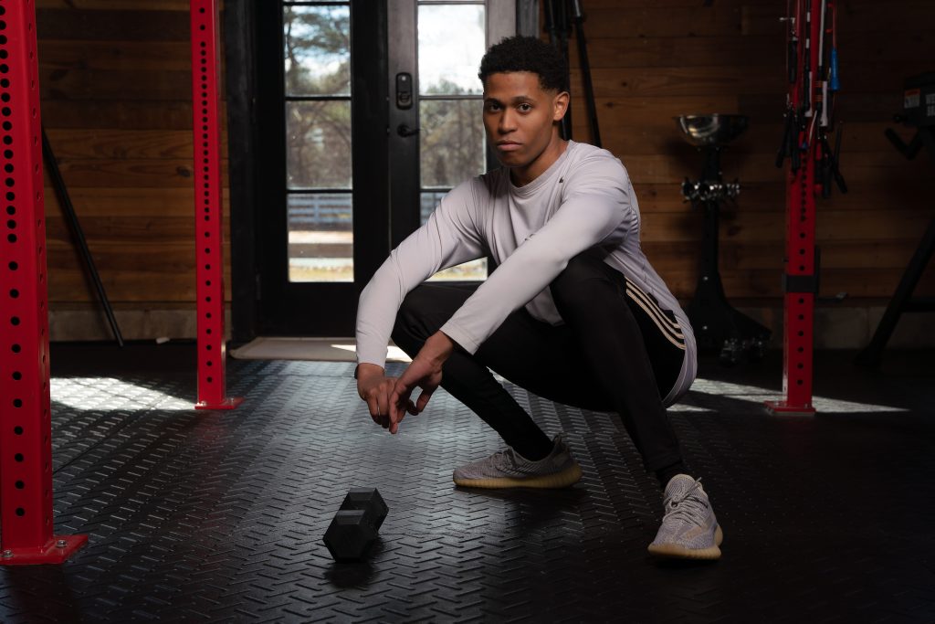 With a focused deep squat pose and a dumbbell by his side, Tyler Jurelle is emphasizing strength and balance. Check out Tyler Jurelle's full portfolio for all men's fashion and lifestyle content.