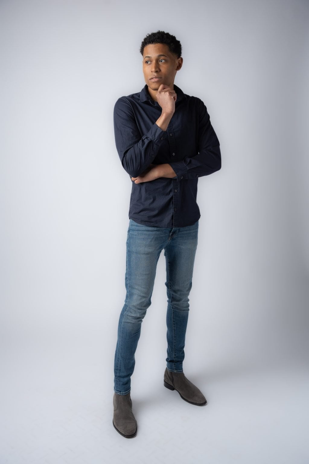 Men's fashion expert Tyler Jurelle is exuding casual confidence in a dark blue button-up shirt, blue jeans, and gray boots.