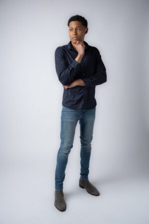 Men's fashion expert Tyler Jurelle is exuding casual confidence in a dark blue button-up shirt, blue jeans, and gray boots.