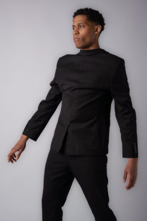Male model Tyler Jurelle is making a fashion statement in a black suit with the blazer worn backward, set against a white backdrop.