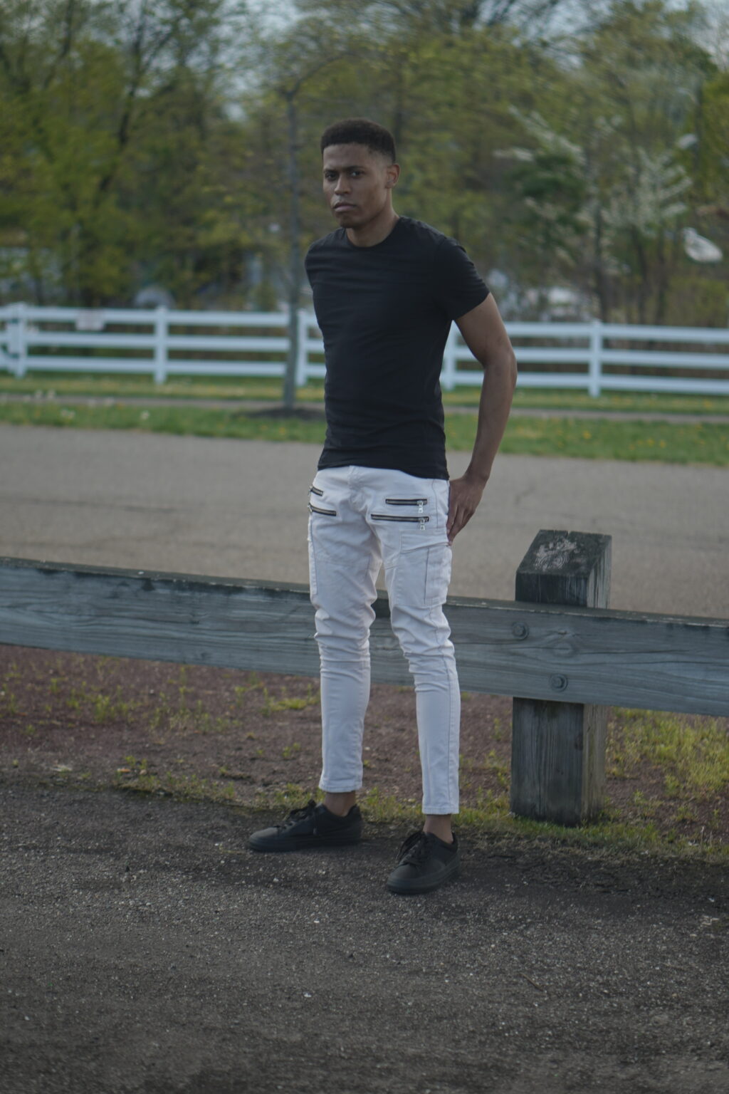 Tyler Jurelle is standing outdoors, showcasing a full-body look in a black t-shirt and light khaki cargo jeans.