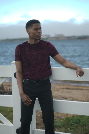 Showcasing urban fashion, Tyler Jurelle is dressed in a burgundy t-shirt and black pants with confidence.