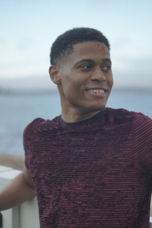 Tyler Jurelle smiles thoughtfully while looking away, wearing a stylish burgundy t-shirt.