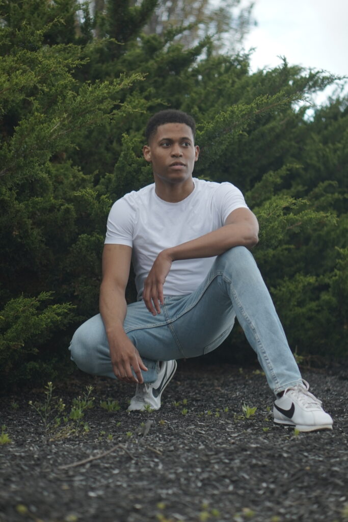 Tyler Jurelle in an athletic squat pose, dressed in light blue jeans and a white t-shirt.