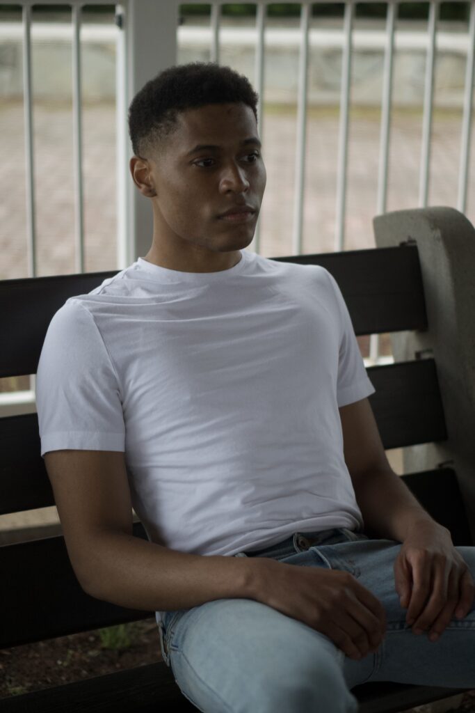 Tyler Jurelle sitting outdoors in a relaxed pose, wearing a white t-shirt and light blue jeans.