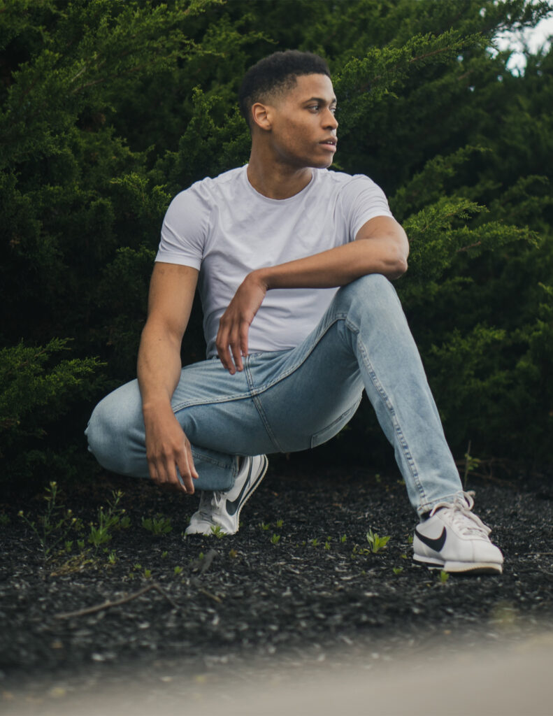 Displaying strength in a deep squat, Tyler Jurelle wears a white t-shirt and light blue jeans.