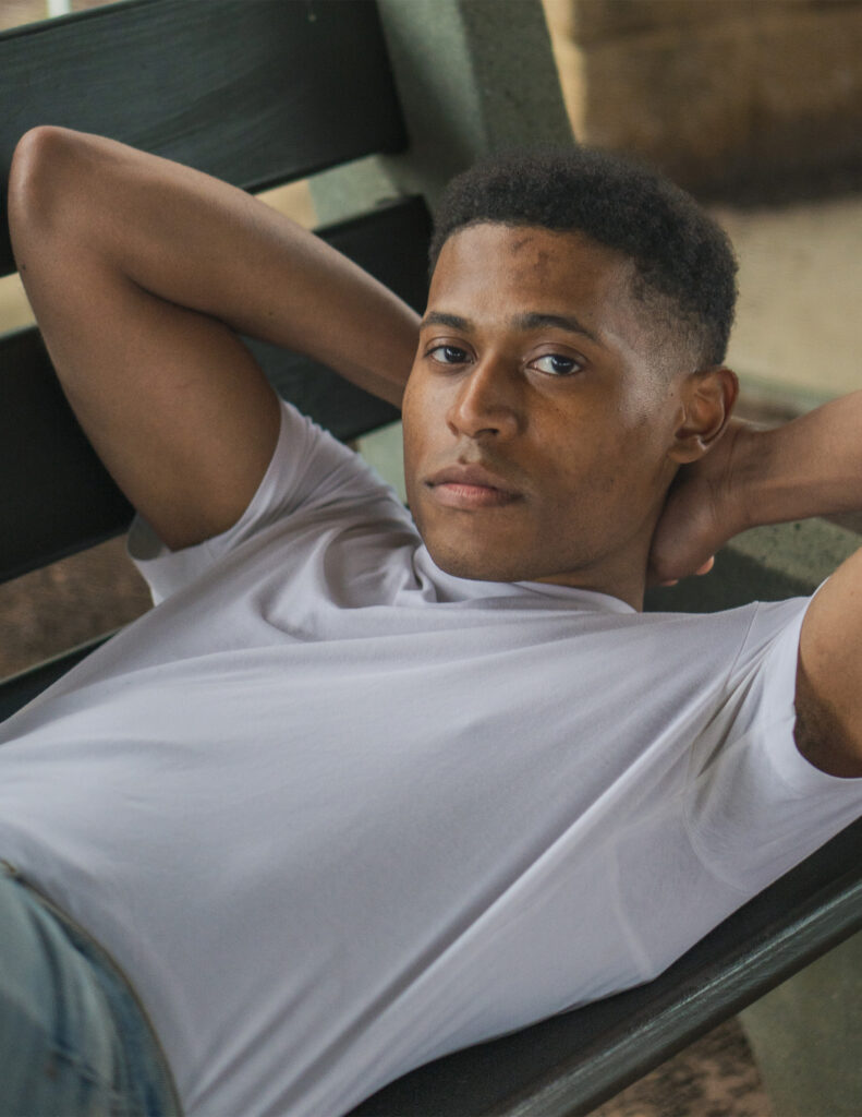 Tyler Jurelle laying on a bench in a close-up shot, wearing a white t-shirt.