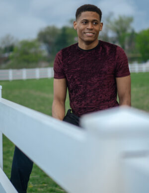 Tyler Jurelle displays effortless charm with a smile, dressed in a burgundy t-shirt and black pants.