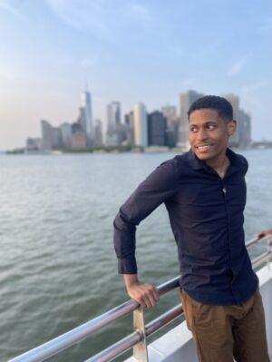 Tyler Jurelle is overlooking the water with the NYC skyline in the background during a break.