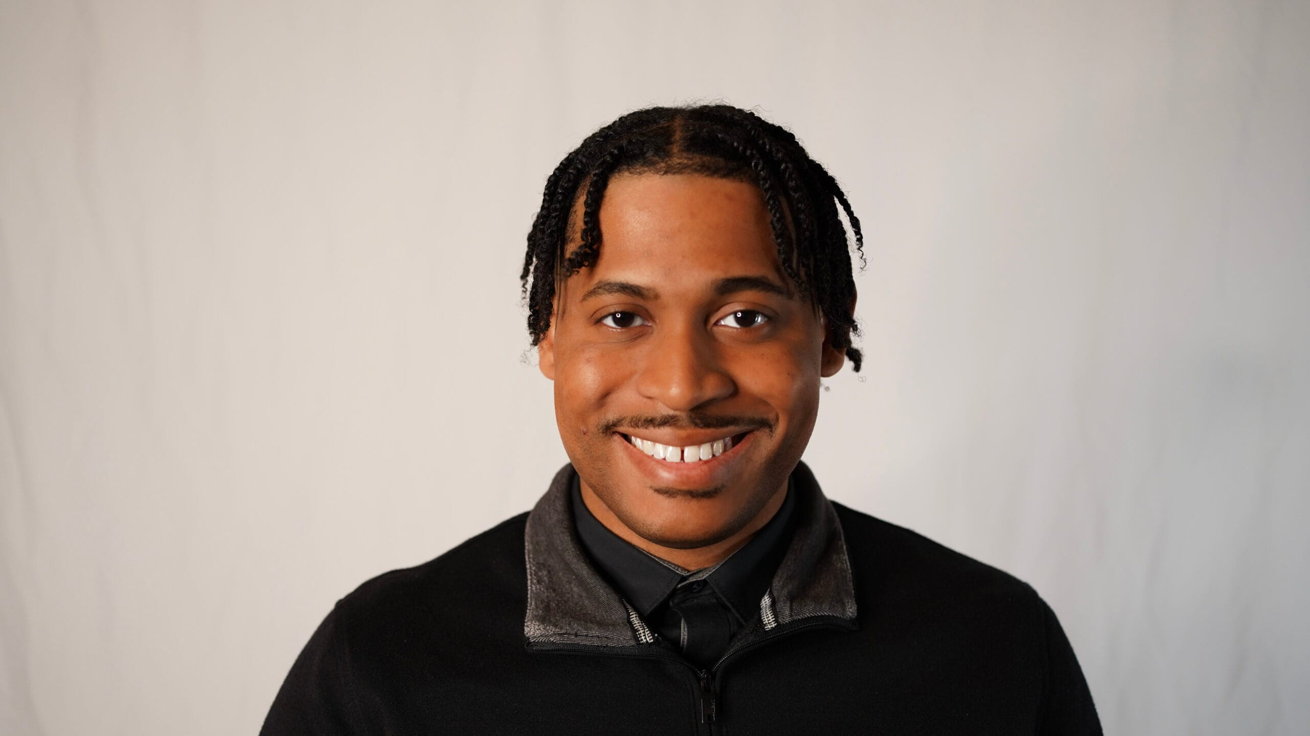 Studio headshot of Tyler Jurelle smiling in a black quarter-zip sweater over a shirt and tie.